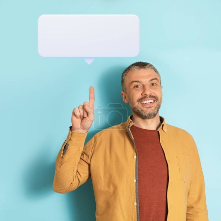 Positive middle aged caucasian man experiencing AHA moment, having creative idea, posing over blue studio background. Mature male gesturing eureka, pointing up at blank speech balloon