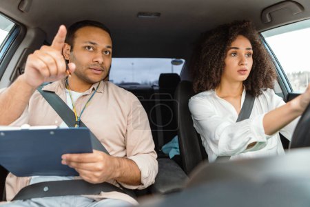 Viaje seguro en coche. Hombre Instructor Árabe Proporcionando Lecciones de Conducción a la Mujer Conductora Aspirante, Navegando por las Reglas de Seguridad Vial y Tráfico, Señalando el dedo en la carretera y sosteniendo el portapapeles