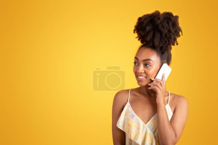 Foto de Feliz milenaria mujer negra llamando por teléfono, pensando, mira el espacio vacío, aislado sobre fondo naranja, estudio. Anuncio y oferta, emociones humanas en tiempo libre, chismes, buenas noticias y comunicación - Imagen libre de derechos