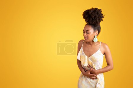 Photo for Sad despaired millennial black lady presses hands to stomach, suffering from belly pain, isolated on orange background, studio. Poisoning, nausea, health problems, human emotions, menstruation - Royalty Free Image