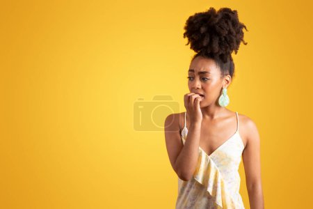 Photo for Sad anxious millennial black lady in dress biting fingers, worried, look at copy space, isolated on orange background, studio. Expect, ad and offer, news, desire and fear human emotions - Royalty Free Image