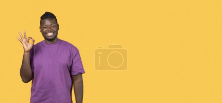 Foto de Estoy bien. Alegre chico negro en púrpura camiseta Gesto OK signo, sonriendo a la cámara de pie sobre el fondo del estudio amarillo. Retrato de la oferta de aprobación de clientes satisfechos. Panorama, Espacio vacío - Imagen libre de derechos
