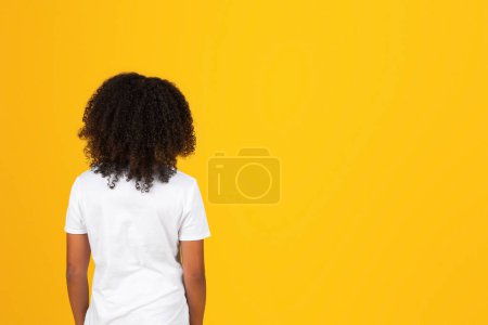 Foto de Adolescente alumna negra en camiseta blanca mira el espacio de copia, aislado sobre fondo amarillo, estudio. Venta y vuelta a la escuela, estudio, publicidad y oferta, estilo de vida, educación - Imagen libre de derechos