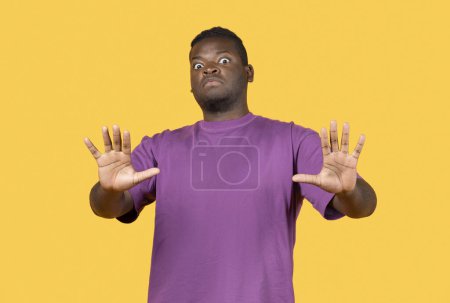 Téléchargez les photos : Choqué jeune homme afro-américain faisant geste d'arrêt avec les mains, repoussant la caméra debout sur fond jaune en studio. Dégoûter, dire non et émotion négative, signe de l'espace personnel - en image libre de droit