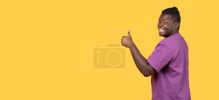 Téléchargez les photos : Super choix. Un jeune Afro-Américain positif gesticulant les pouces vers le haut à la caméra sur fond jaune. Heureux homme millénaire recommandant quelque chose comme. Panorama, espace de copie - en image libre de droit