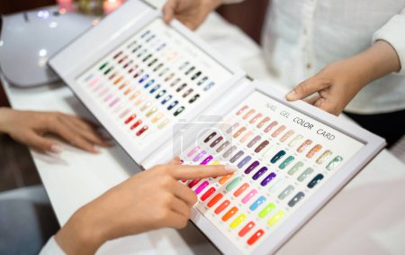 Photo for Trendy Nail Color Choice. Closeup of Client Lady Choosing Colorful Fingernail Design With Professional Manicurist, Pointing At Nail Gel Color Card At Beauty Salon Indoor, Cropped Shot - Royalty Free Image
