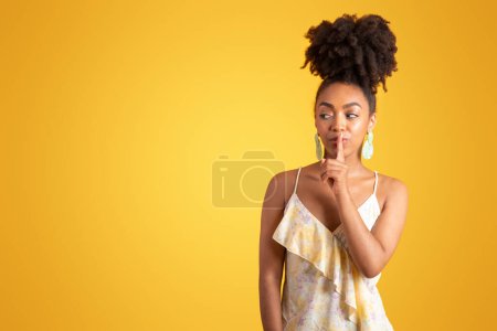Foto de Serious confidente milenaria dama negra en vestido presiona el dedo a los labios, hace shhh signo, aislado sobre fondo naranja, estudio. Sorpresa, anuncio y oferta, noticias, chismes y emociones humanas - Imagen libre de derechos