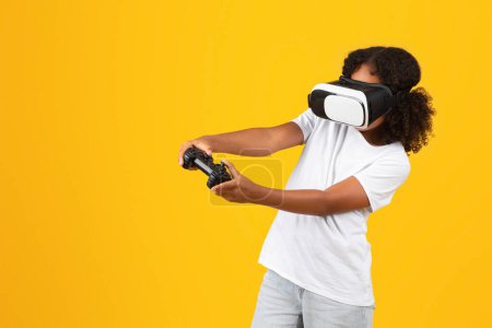 Foto de Adolescente positiva alumna negra en camiseta blanca, gafas VR con joystick disfruta de tiempo libre, jugando juego en línea aislado en el fondo amarillo, estudio. Gadget para la diversión, estilo de vida - Imagen libre de derechos