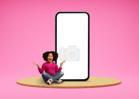 Photo for Surprised Black Little Girl Sitting Near Big Blank Smartphone With White Screen, Excited African American Female Child Advertising New Mobile App Or Online Offer, Posing On Pink Background, Mockup - Royalty Free Image