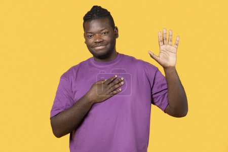 Photo for I Swear. Honest Black Man Doing Oath Gesture Posing In Purple T Shirt, Looking At Camera Standing Over Yellow Background In Studio. Guy Presses Hand to Chest and Swears. Gratitude, Promise Concept - Royalty Free Image