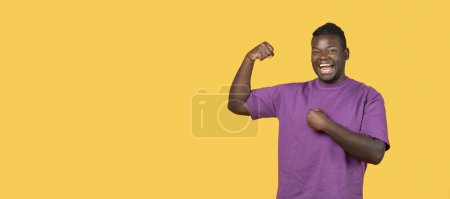 Photo for Strength And Victory. Joyful Black Guy Showing Biceps Muscles On Hand And Gesturing Yes In Joy, Standing Over Yellow Studio Background, Smiling To Camera. Panorama With Copy Space - Royalty Free Image