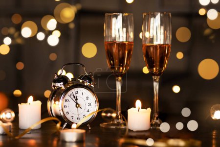 Foto de Reloj viejo, dos copas con champán y velas blancas encendidas en la mesa sin gente alrededor sobre el fondo de las luces. Año Nuevo 2024 víspera concepto de celebración - Imagen libre de derechos