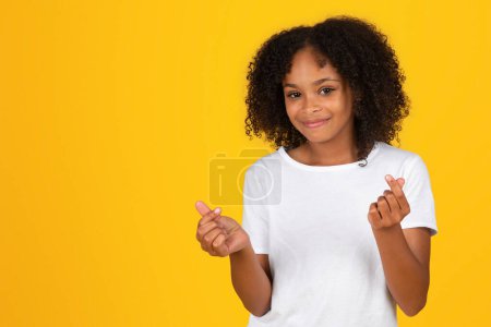 Téléchargez les photos : Adolescente noire souriante en t-shirt blanc claque des doigts, profitez de bonnes nouvelles, isolée sur fond jaune, studio. Grand panneau d'étude, vente et retour à l'école, annonce et offre, mode de vie, éducation - en image libre de droit