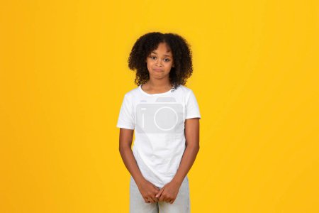 Téléchargez les photos : Calme triste offensé adolescent afro-américaine en t-shirt blanc, isolé sur fond orange, studio. Les émotions humaines, l'étude et la connaissance, les problèmes de l'éducation scolaire moderne - en image libre de droit