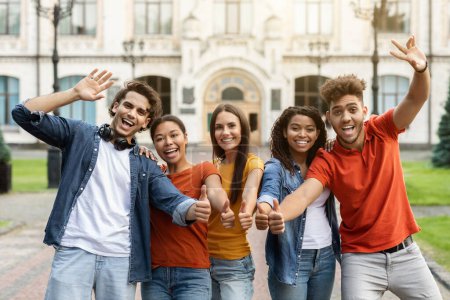 Photo for We Recommend. Group Of Cheerful Multiethnic Students Gesturing Thumbs Up At Camera While Posing Outdoors, Happy Young College Friends Recommending Educational Or Tuition Program, Enjoying Study - Royalty Free Image