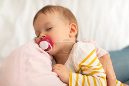 Photo for Adorable infant girl on mothers hands sucking pacifier and sleeping peacefully, above view, closeup. Mother holding baby daughter. Motherhood, maternity concept - Royalty Free Image