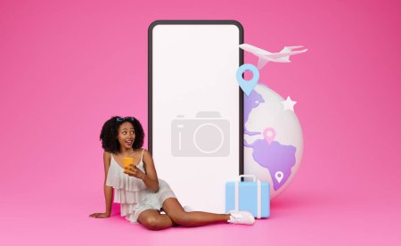 Téléchargez les photos : Curieux étonné jolie jeune femme noire en tenue d'été assis sur le sol par un téléphone énorme avec écran blanc, fond rose, concept de voyage, réservation en ligne de vacances, offre de voyage, maquette - en image libre de droit