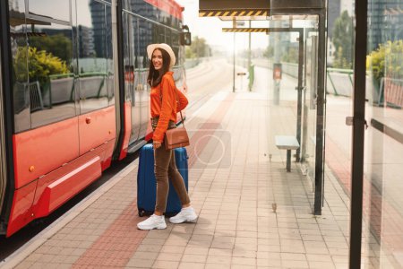 Photo for Urban Commute, Transportation. Smiling Traveler Woman Boarding a Modern Tram at Outdoor Station with Suitcase. Public Transport Adventure in City. Full Length Shot, Empty Space For Text - Royalty Free Image