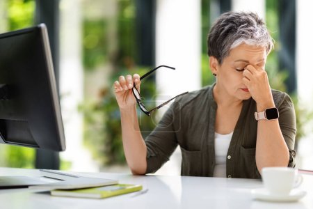 Photo for Tired exhausted middle aged businesswoman sitting at workplace at home office, rubbing eyes, holding eyeglasses. Overworked mature lady suffering from migraine, bad vision, have headache - Royalty Free Image