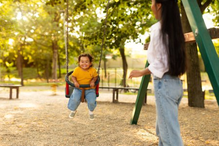 Foto de Aventuras de tiempo de juego. Asiática mamá balanceo su bebé niño hija en swing al aire libre en el parque, selectivo foco en alegre bebé disfrutando de patio de recreo divertido y feliz momentos con la madre - Imagen libre de derechos