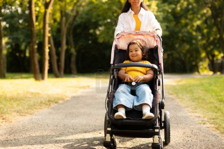 Foto de Curiosa niña asiática disfrutando de caminar con mamá mientras está sentada en el paseo en Green Park. Mujer irreconocible paseando con su pequeña hija fuera, tiro recortado - Imagen libre de derechos