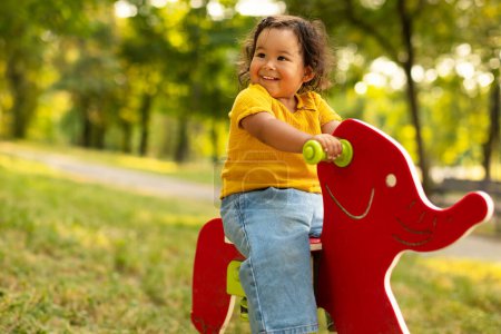 Photo for Toddler Joy. Cheerful Japanese Baby Toddler Girl Riding Coil Spring Elephant at Outdoor Playground in Amusement Park, Smiling Looking Aside, Enjoying Playtime Alone. Free Space - Royalty Free Image