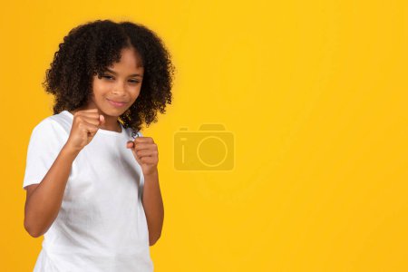 Foto de Sonriente chica afroamericana adolescente fuerte y confiada en camiseta blanca, mostrar puños, luchar, listo para perforar, aislado sobre fondo naranja, estudio. Autodefensa, deportes y bullying, estudio - Imagen libre de derechos