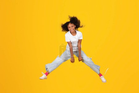 Photo for Happy excited adolescent african american girl in white t-shirt jump, freezes in air, has fun, isolated on orange background, studio. Sale, human emotions, lifestyle, study and knowledge, freedom - Royalty Free Image