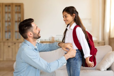 Photo for Back to School. Happy father preparing little schoolgirl daughter for first school day, helping to put on bag at home interior. Education and study preparation, daddy and kid girl bond concept - Royalty Free Image