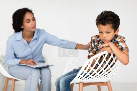 Photo for Child Depression. School Pscyhologist Lady Comforting Unhappy Kid Boy During Psychotherapy Session Sitting Indoor. Depressed Schoolboy Visiting Psychotherapist Having Mental Issues. Selective Focus - Royalty Free Image