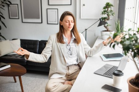 Téléchargez les photos : Office zen. Femme d'affaires européenne calme méditant les yeux fermés, assise sur le lieu de travail en position de lotus. Dame détendue se sentant paisible et équilibrée - en image libre de droit