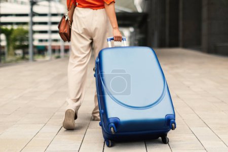 Téléchargez les photos : Offre de voyage. Prise de vue recadrée de voyageur femme marchant avec valise à l'aéroport moderne en plein air, Retour à la caméra. Dame passager méconnaissable en voyage de vacances avec son sac à bagages - en image libre de droit