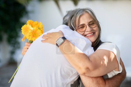 Photo for Happy old european husband and wife hugging with bouquet of flowers, celebrating anniversary, holiday, enjoy spare time, outdoor, close up. Family relationship and date together, romantic - Royalty Free Image