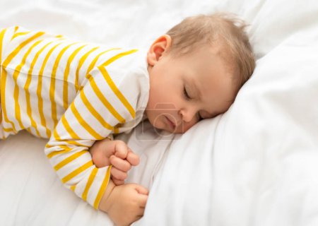 Foto de Cuna de sueños. Los bebés duermen tranquilamente en una cama acogedora, un niño acostado en un juego de ropa de cama blanca, primer plano, espacio libre. Confort para el niño, dulce sueño y sueños, infancia - Imagen libre de derechos