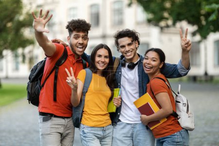 Téléchargez les photos : Heureux étudiants multietnic joyeux posant ensemble à l'extérieur, Groupe d'amis souriants de collège joyeux avec des sacs à dos et des cahiers de travail se détendre après les cours, rire et gesticuler à la caméra - en image libre de droit