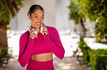 Photo for Favorite Song. Portrait of happy young sportive black lady wearing wireless headphones listening to music while exercising at park. Lady enjoying playlist for workout, looking at copy space - Royalty Free Image