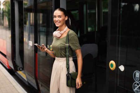 Photo for Connected Commute. Joyful Passenger Young Lady Exiting Tram, Texting and Browsing Internet on Phone, Using Mobile Application Booking Train Ride. Urban Public Transportation Concept - Royalty Free Image