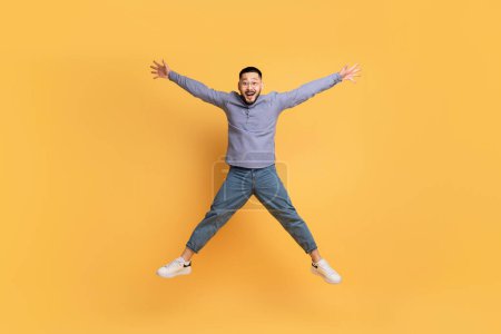 Foto de Ventas locas. Divertido hombre asiático saltando como una estrella sobre fondo amarillo, tipo despreocupado Millennial esparciendo brazos y piernas y mirando a la cámara, engañando y divirtiéndose, longitud completa con espacio de copia - Imagen libre de derechos