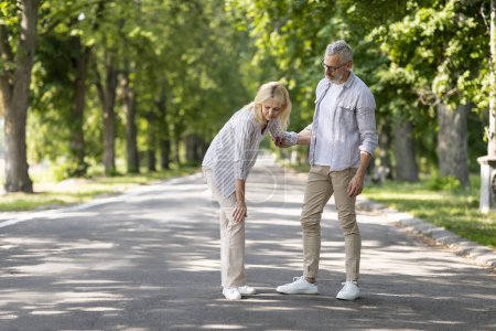Photo for Senior Woman Suffering Knee Injury While Walking In Park With Husband, Upset Mature Female Having Osteoarthritis, Standing On Path And Rubbing Painful Area, Caring Man Supporting Wife, Copy Space - Royalty Free Image