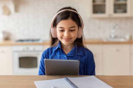 Photo for E-Learning Offer. Portrait Of Cute Preteen Girl In Wireless Earphones Using Digital Tablet, Doing Homework Online While Sitting At Desk At Home, Schoolgirl Websurfing On Tab Computer Studying - Royalty Free Image