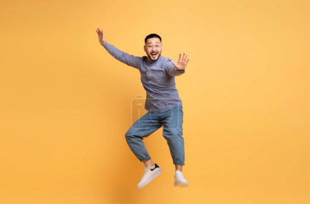 Foto de Alegre joven asiático hombre engañando sobre amarillo fondo, positivo divertido millennial chico en casual ropa saltar en el aire y mirando a cámara, divertirse en estudio, longitud completa, copiar espacio - Imagen libre de derechos