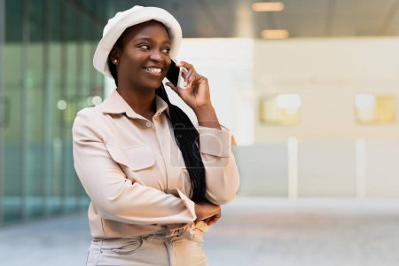 Photo for Happy pretty young black woman in stylish casual outfit have phone conversation on the street. Positive african american student talking on smartphone and smiling, copy space. Communication concept - Royalty Free Image