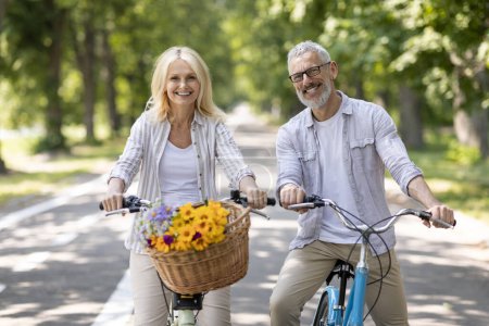 Téléchargez les photos : Portrait de couple mature positif faisant du vélo ensemble dans un parc d'été, heureux conjoints aînés joyeux souriant à la caméra, posant à l'extérieur tout en faisant du vélo, s'amusant, jouissant d'un mode de vie actif - en image libre de droit