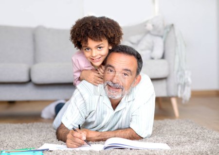 Photo for Talent And Fun. Cheerful Grandson Cuddling With Grandfather While Sketching Together At Home, Smiling To Camera, Posing With Sketchbook And Pencils In Modern Living Room Interior - Royalty Free Image