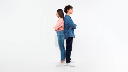 Photo for Troubled Relationship Issue. Unhappy Young Couple After Quarrel Crossing Hands Standing Back To Back, Offended After Conflict Over White Studio Background. Girlfriend And Boyfriend Breaking Up - Royalty Free Image
