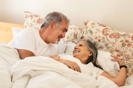 Téléchargez les photos : Souriant heureux vieux mari caucasien se réveille femme au lit, profiter de bonne matinée ensemble dans l'intérieur de la chambre. Week-end et temps libre, relation et amour, mode de vie, repos, détente - en image libre de droit