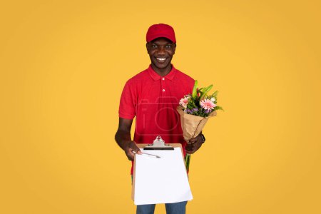 Photo for Cheerful millennial african american guy courier hold bouquet of flowers, gives clipboard for sign, isolated on orange studio background. Delivery of gift at home, work and service for holiday - Royalty Free Image