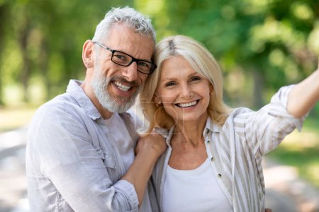 Happy beautiful mature couple posing for selfie together outdoors, cheerful senior man and woman talking photo while walking in park, smiling and looking at camera, enjoying date outside, closeup