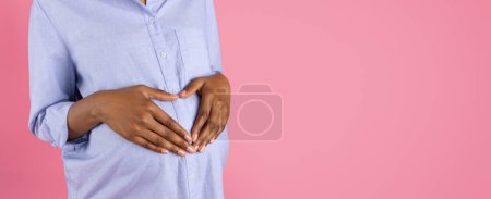 Photo for Young black pregnant woman puts heart shape hands on big belly, isolated on pink studio background, panorama, cropped. Expect baby, love lifestyle, future motherhood, fertility - Royalty Free Image