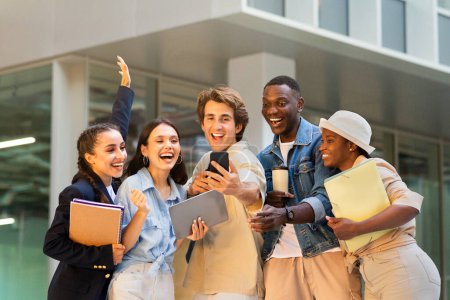 Photo for Multiracial group of students happy young men and women with gadgets and books in their hands taking selfie on smartphone at campus next to university building, friends having fun after classes - Royalty Free Image